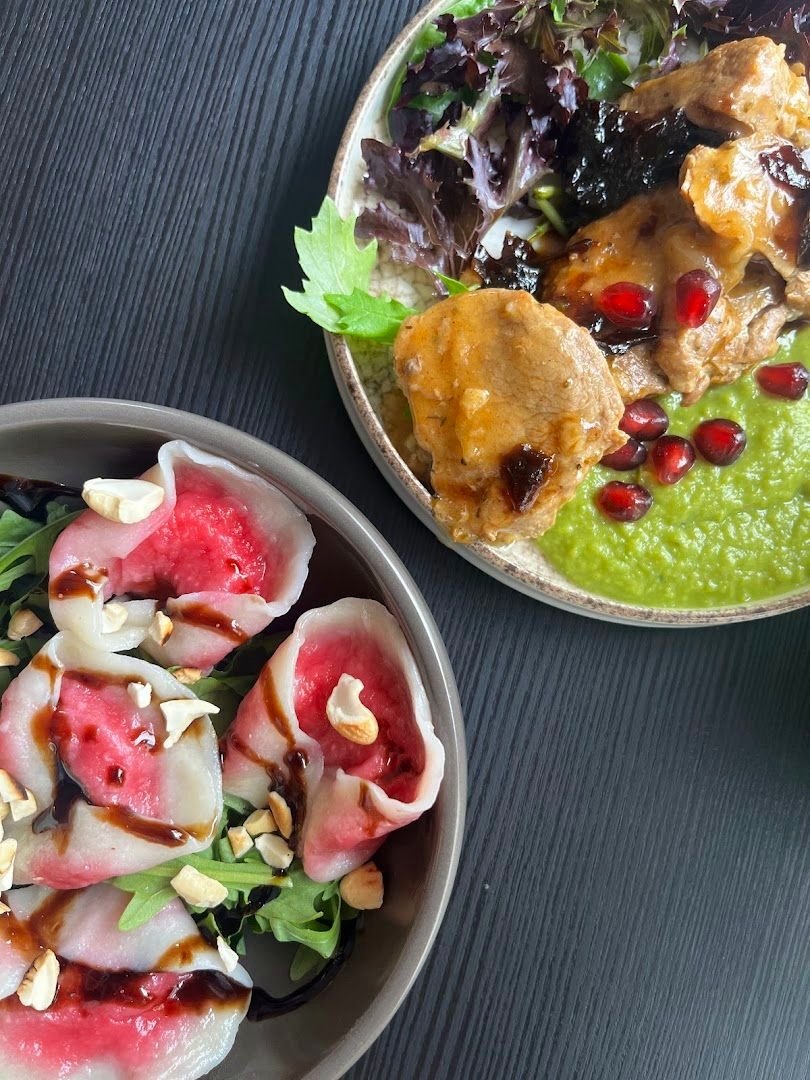Two small plates on a dark table, one with pomegranate seeds over a bright green purée